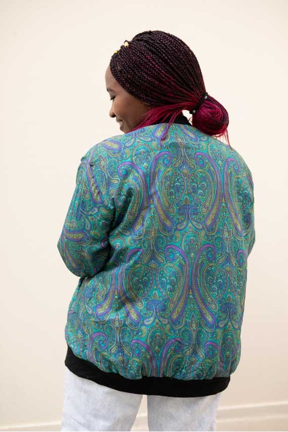 Vista trasera de chaqueta bomber paisley turquesa y violeta con estampado ornamental de inspiración sari.