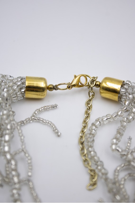 Cierre metálico dorado con cadena ajustable de un collar de cuentas plateadas. Cierre metálico dorado con cadena ajustable de un collar de cuentas plateadas.