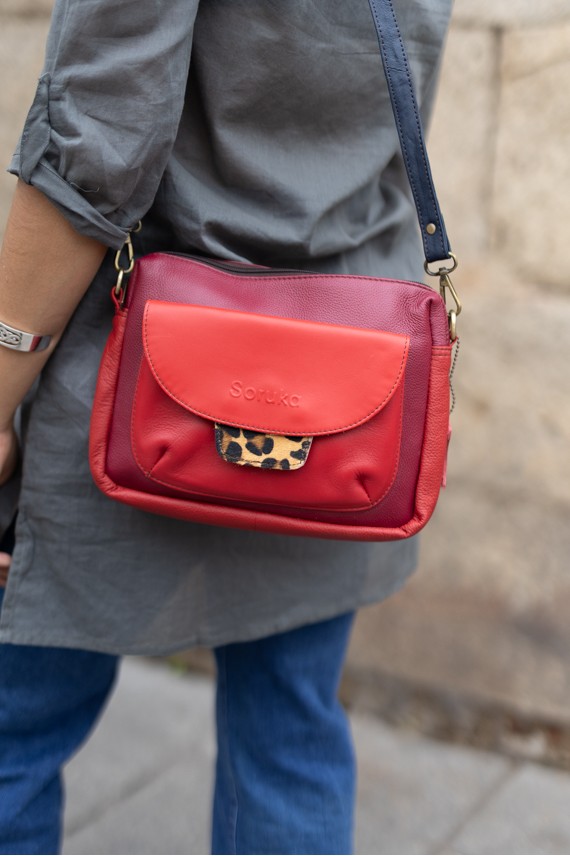 “Bolso Cher Soruka de piel reciclada en colores verde, azul y rojo, diseño artesanal sostenible con lengüeta reversible.”
