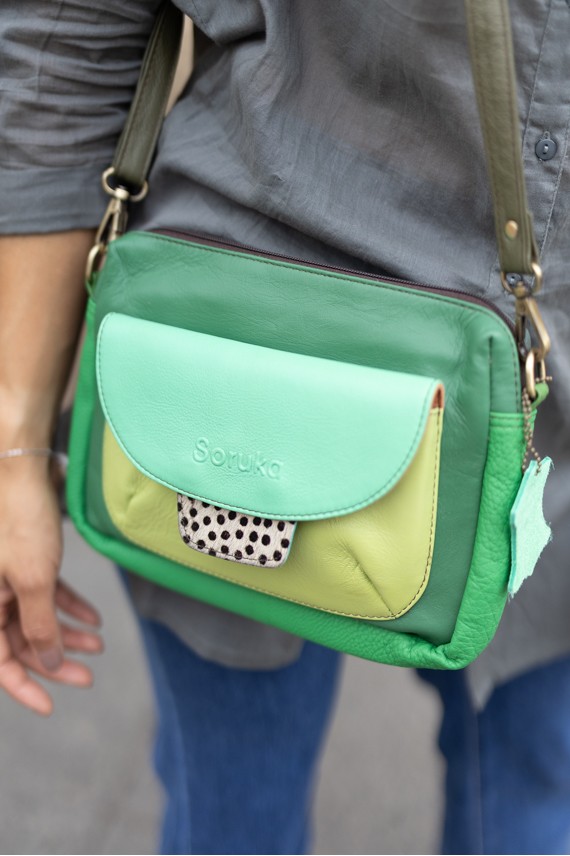 “Bolso Cher Soruka de piel reciclada en colores verde, azul y rojo, diseño artesanal sostenible con lengüeta reversible.”
