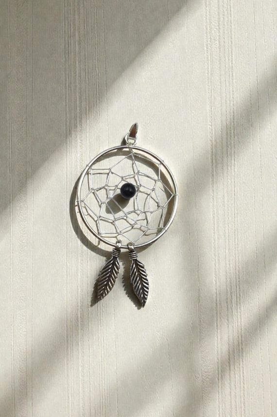 Colgante artesanal tipo atrapasueños con entramado metálico, piedra central y dos plumas colgantes