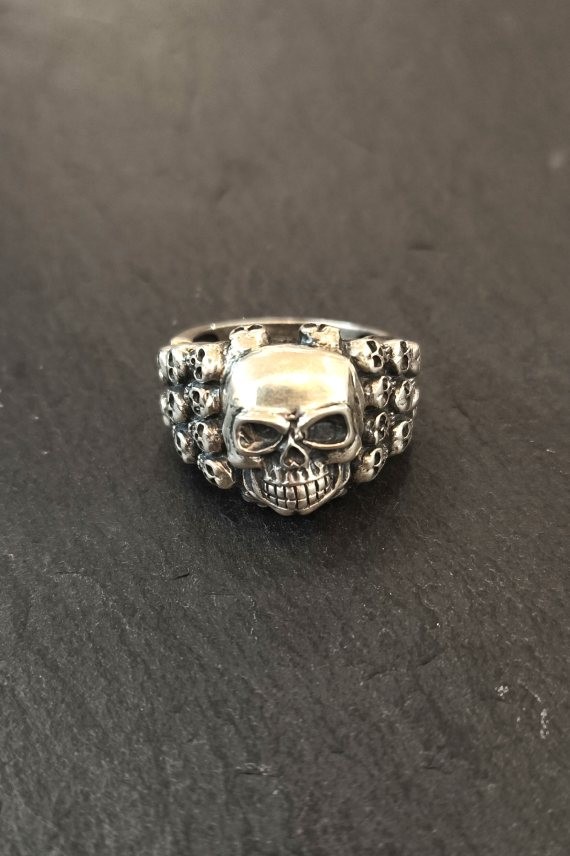 Anillo plateado con calavera central y laterales decorados con pequeñas calaveras