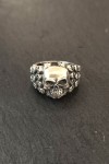 Anillo plateado con calavera central y laterales decorados con pequeñas calaveras