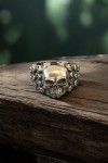 Anillo plateado con calavera central y laterales decorados con pequeñas calaveras
