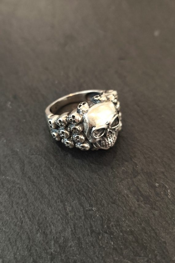 Anillo plateado con calavera central y laterales decorados con pequeñas calaveras
