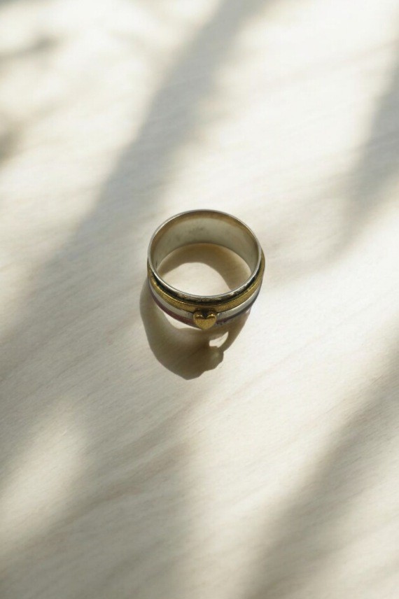 Anillo de plata con base grabada con motivos florales y tres franjas giratorias en tonos dorado, plateado y plata rosada.