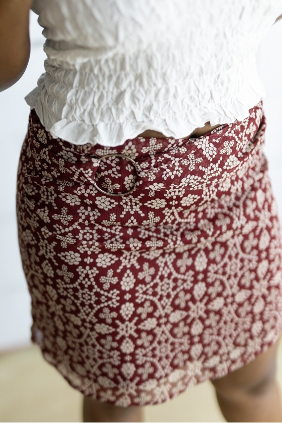 Falda corta burdeos con estampado floral beige y cinturón integrado con hebilla metálica, prenda boho chic para mujer.