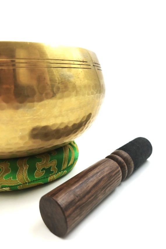 Cuenco tibetano artesanal de latón con mazo de madera y cojín decorativo para meditación, yoga y relajación.