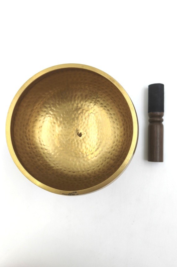 Cuenco tibetano artesanal de latón con mazo de madera y cojín decorativo para meditación, yoga y relajación.