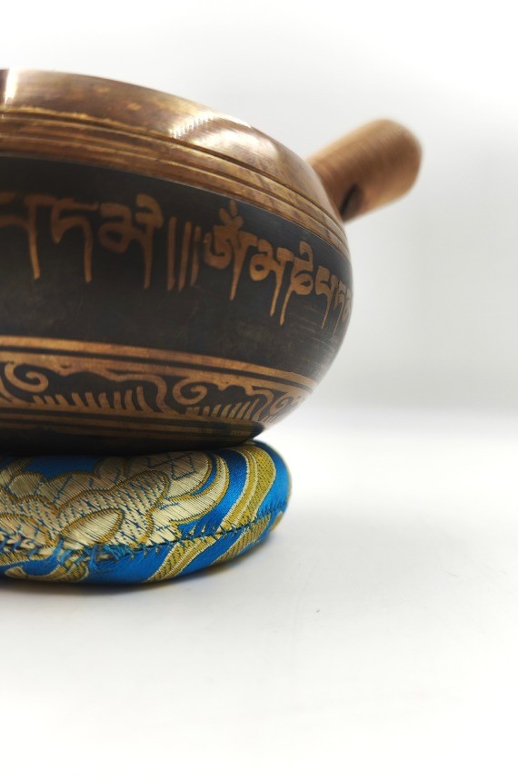 Cuenco tibetano artesanal con símbolo Om Mani, mantras grabados, mazo de madera y cojín decorativo para meditación y relajación.