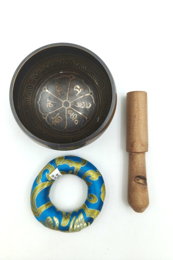 Cuenco tibetano artesanal con símbolo Om Mani, mantras grabados, mazo de madera y cojín decorativo para meditación y relajación.