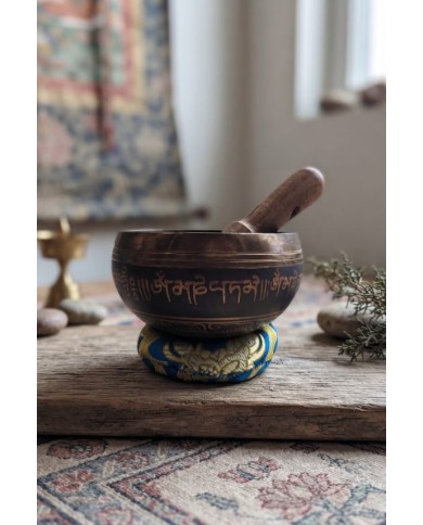 Cuenco tibetano artesanal con símbolo Om Mani, mantras grabados, mazo de madera y cojín decorativo para meditación y relajación.