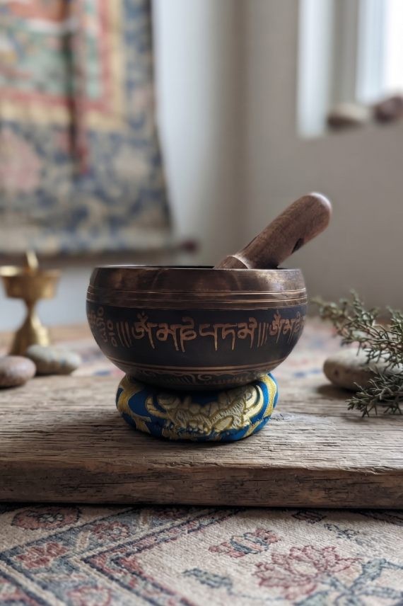 Cuenco tibetano artesanal con símbolo Om Mani, mantras grabados, mazo de madera y cojín decorativo para meditación y relajación.