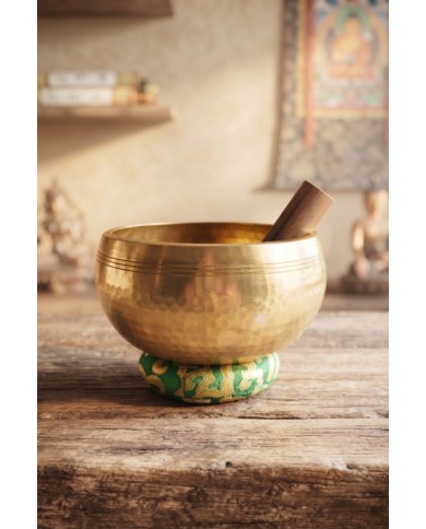 Cuenco tibetano artesanal de latón con mazo de madera y cojín decorativo para meditación, yoga y relajación.