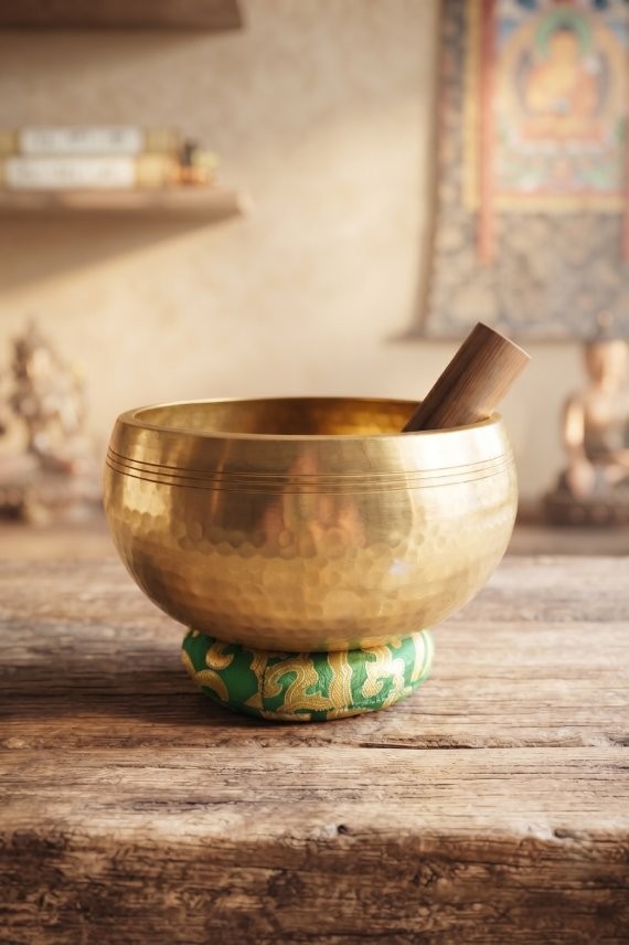 Cuenco tibetano artesanal de latón con mazo de madera y cojín decorativo para meditación, yoga y relajación.