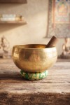 Cuenco tibetano artesanal de latón con mazo de madera y cojín decorativo para meditación, yoga y relajación.