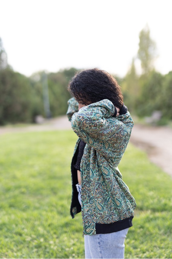 Vista lateral de chaqueta bomber de seda estampada en tonos verde agua, turquesa y azul.