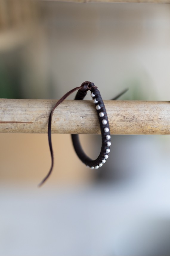 Pulsera artesanal Sol de cuero marrón con cuentas plateadas y cierre mediante cordones.