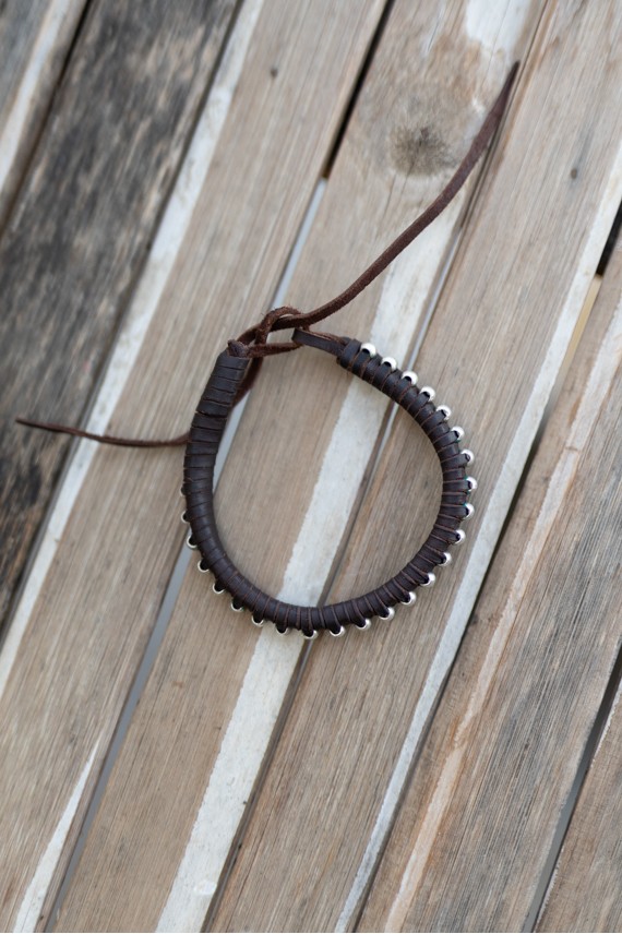 Pulsera artesanal Sol de cuero marrón con cuentas plateadas y cierre mediante cordones.