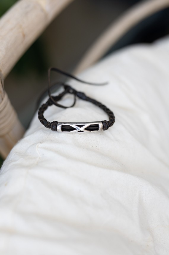 Pulsera Travesía de cuero oscuro trenzado con pieza metálica plateada y líneas entrelazadas.