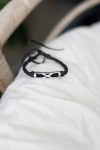 Pulsera Travesía de cuero oscuro trenzado con pieza metálica plateada y líneas entrelazadas.
