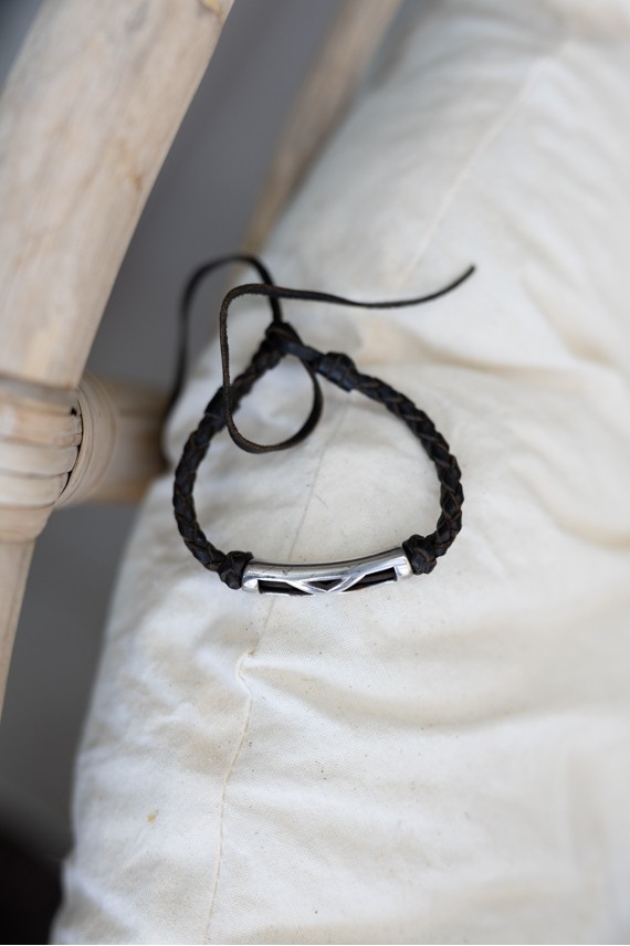 Pulsera Travesía de cuero oscuro trenzado con pieza metálica plateada y líneas entrelazadas.