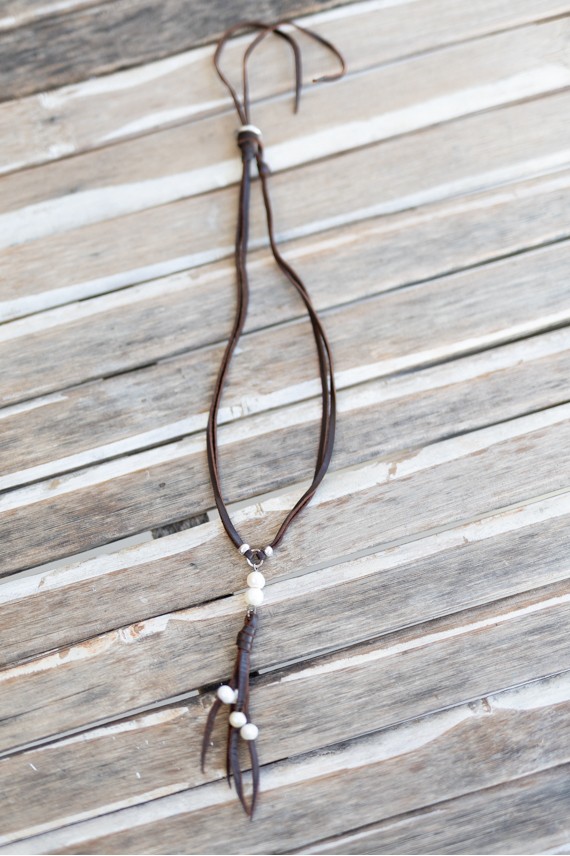 Collar de cuero marrón con perlas, colgante de tiras y cierre regulable con botón.