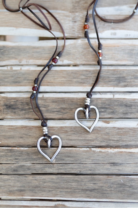 Detalle de collar de cuero con gran corazón abierto plateado y gemas circulares de colores.