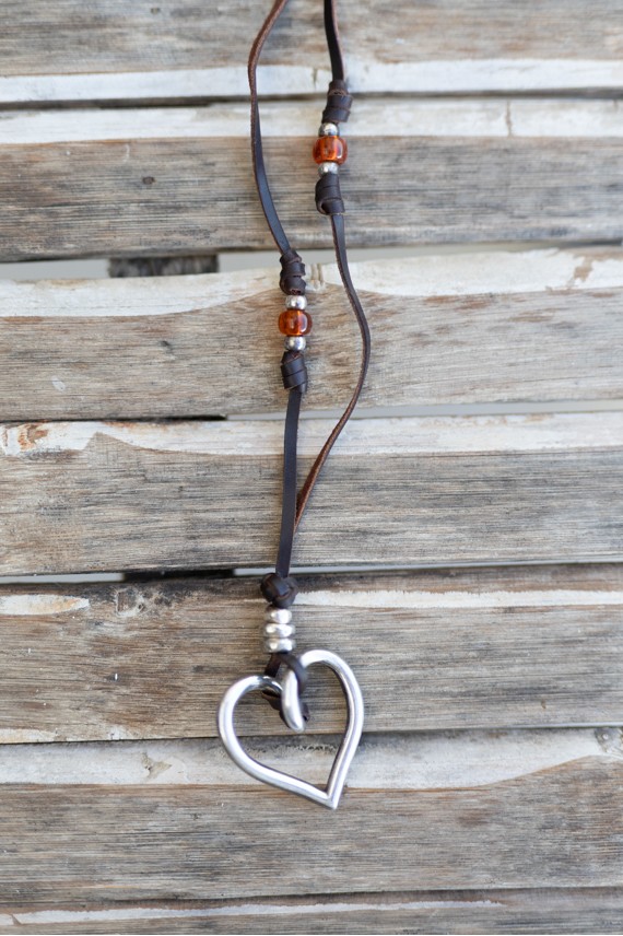 Collar boho de cuero con corazón plateado, detalles metálicos y gemas en tonos ámbar y rojizos.