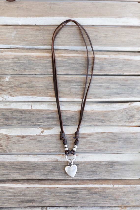Detalle de collar de cuero con corazón de zamak, aro central y bolas plateadas decorativas.