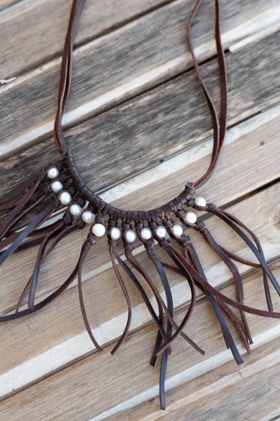 Detalle de collar artesanal de cuero marrón con hilera de perlas blancas y flecos largos de estilo boho.