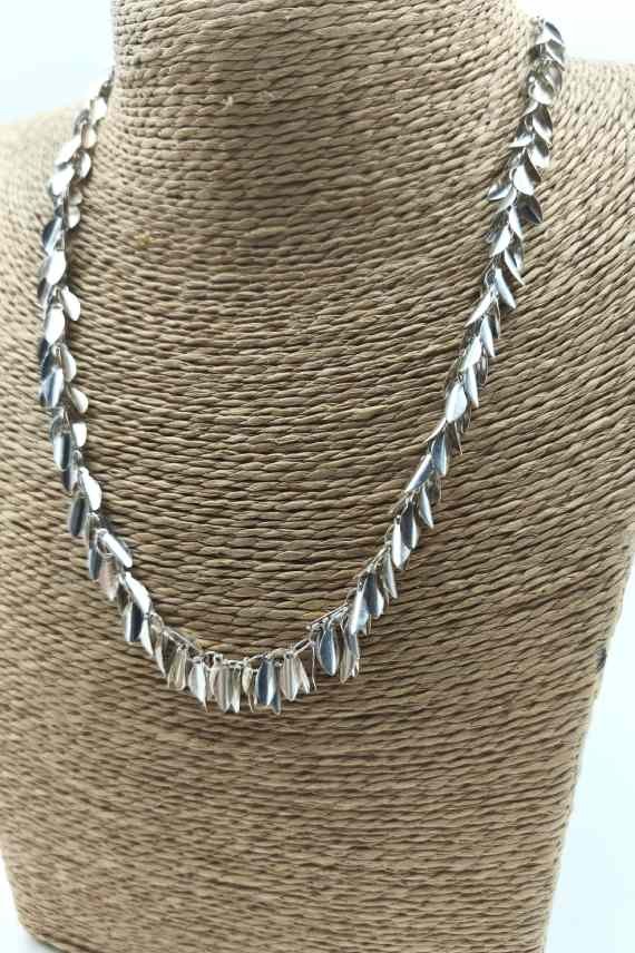 Detalle de collar plateado de latón con pequeñas hojas móviles dispuestas en forma de rama o espiga.