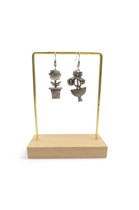 Detalle de pendientes de zamak plateado con diseños diferentes de flor en maceta y ramo floral, estilo boho vintage.