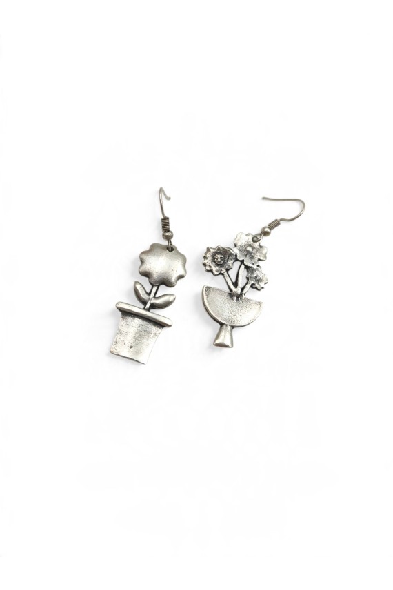 Detalle de pendientes de zamak plateado con diseños diferentes de flor en maceta y ramo floral, estilo boho vintage.
